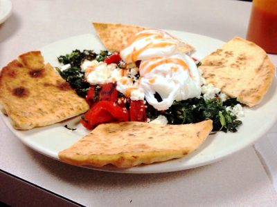 Aidans Way. This picture did pics two poached eggs served on top of a bed of sautéed spinach and roasted peppers, accompanied with a toasted pita cut into four triangular pieces on top of a plate Served on Johny’s original white counter