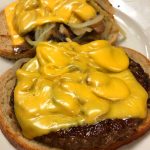 Big Buster. This picture depicts to beef patties Served open face on grilled Ryebread with sautéed mushrooms and onions and melted American cheese on a white plate on Johnys countertop