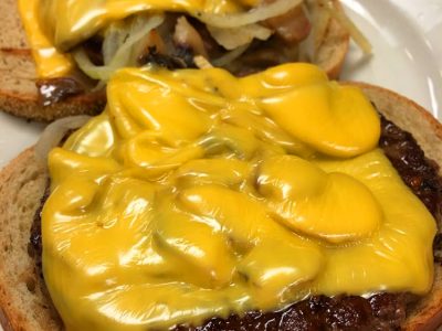 Big Buster. This picture depicts to beef patties Served open face on grilled Ryebread with sautéed mushrooms and onions and melted American cheese on a white plate on Johnys countertop