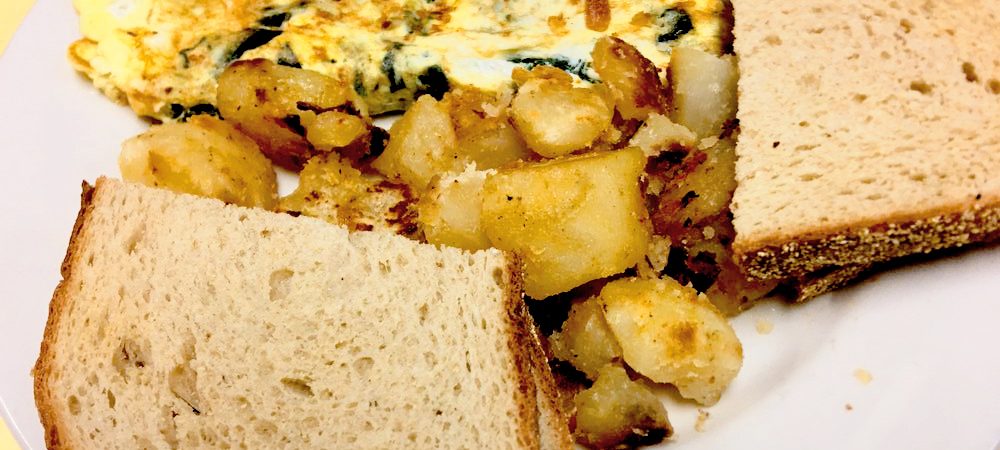 Florentine Omelette. This picture depicts the omelette that consists of spinach and feta cheese accompanied by home fried potatoes and toast served on a white platter on Johnys counter top