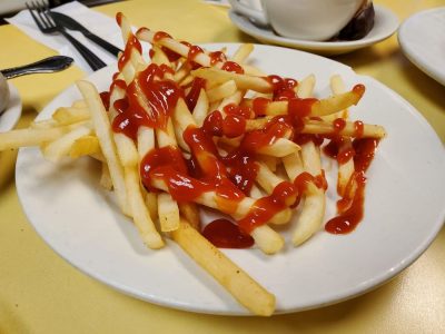 French Fries. This picture shows an order of shoestring french fries topped with ketchup served on a white platter on Johnny’s yellow countertop. With a cuppa coffee on the side for an extra charge