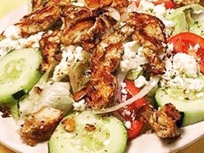 Greek Salad grilled chicken. This picture depicts a salad that it consists of lettuce tomato, peppers, onions, sliced cucumber, feta cheese, chopped grilled chicken and Kalamata olives served on a white platter on Johnys countertop