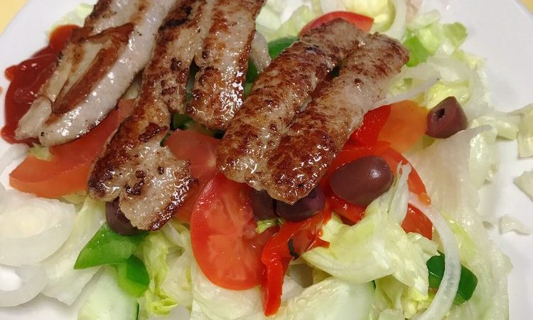 House salad. This picture is the pics a salad that consists of lettuce, tomato, roasted peppers, onions, Kalamata olives on a white plate served with Sausage on top which is an additional charge.