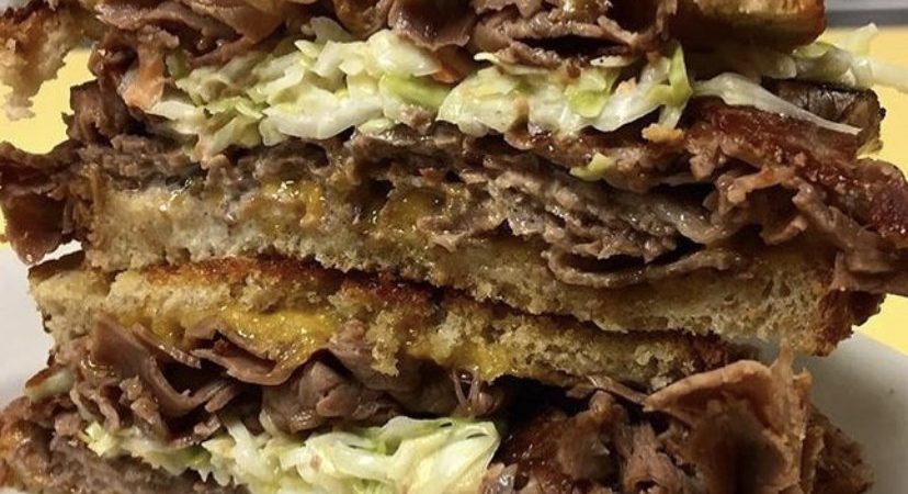 Mr. Moses. Just picture Depicts hot roast beef, homemade coleslaw and melted cheddar cheese on grilled Ryebread that is stacked up one on top of each other on a white platter served on Johnys Luncheonette counter