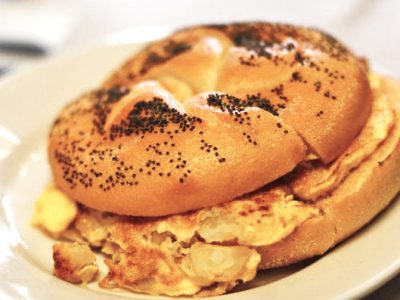 Potato and Egg on a Roll. This picture depicts a sandwich that consists of egg and potato combined, on a Kaiser roll that is cut in half on top of a plate Served on Johny’s’s counter top