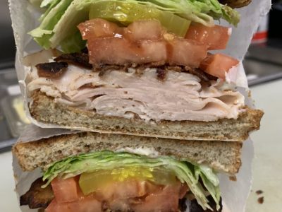 Turkey Club Sandwich. This picture depicts a sandwich that consist of sliced turkey, lettuce and tomato, Bacon Served on Sliced and Toast that is cut in half and placed one on top of another.
