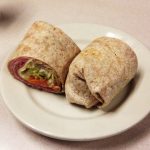 basic wrap sandwich. This picture to pics a basic wrap sandwich that would usually be served on a whole wheat were playing rap that consists of a wide array of meats veggies and cheeses. It is cut in half and served on a white bladder on Johnny’s original Counter top